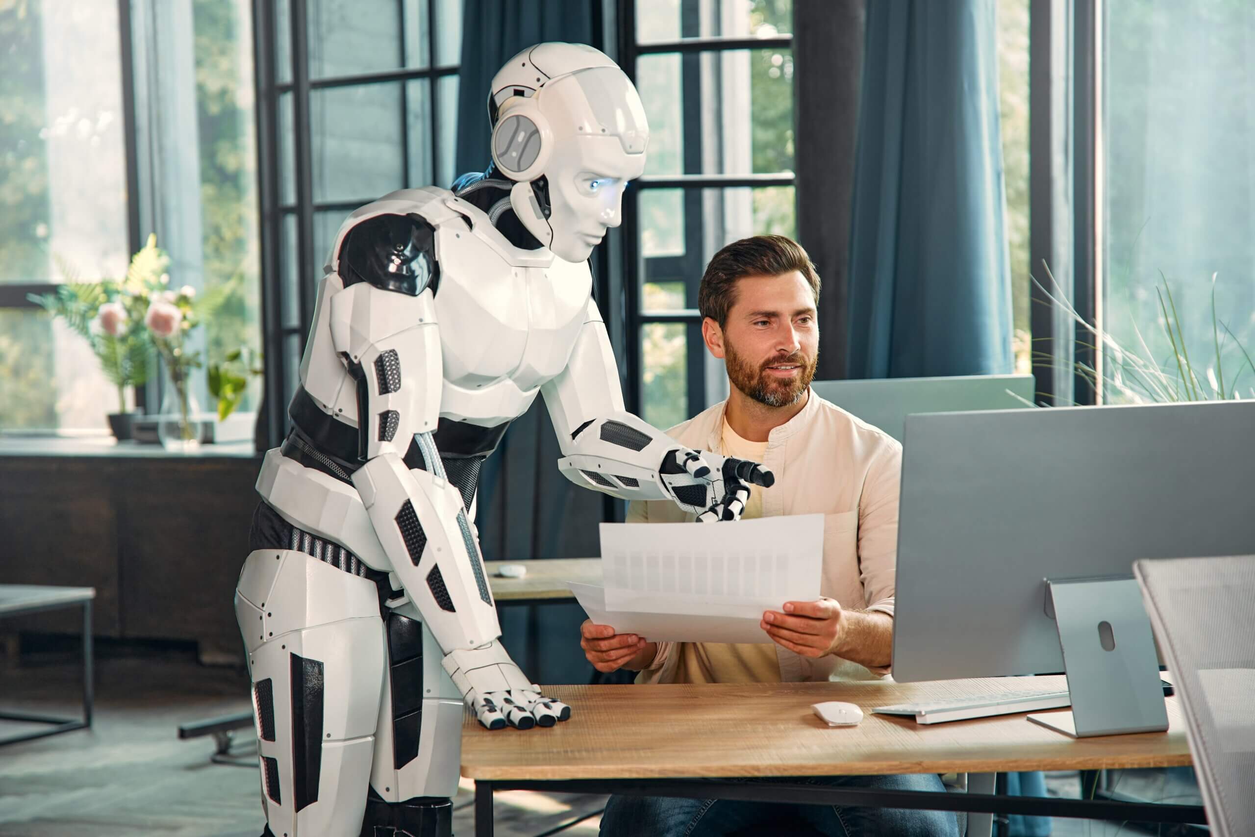 Robot and young businessman working at a computer in a modern office. Collaboration between humans and artificial intelligence.