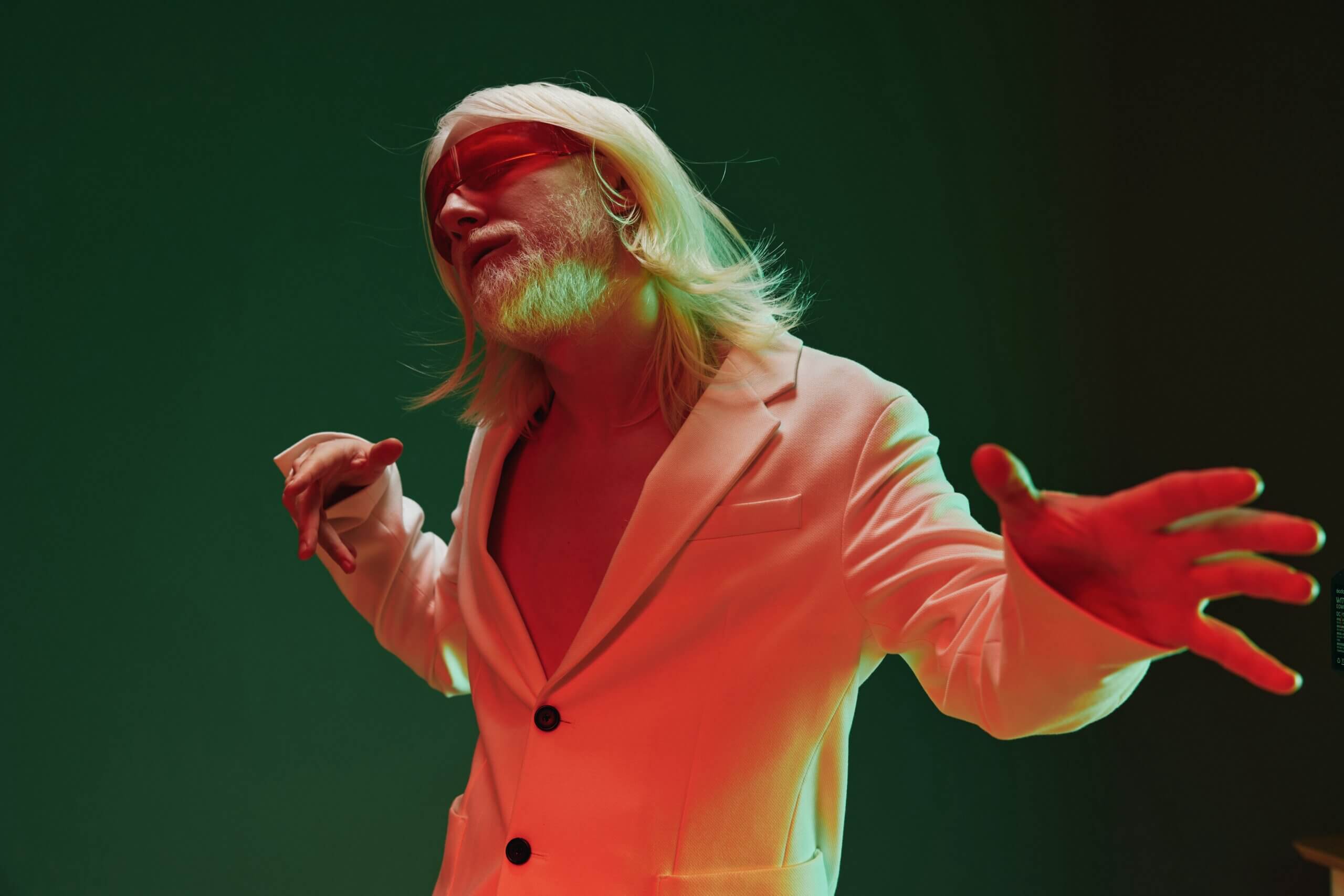 A fashionable man with long blonde hair and a beard conveys deep emotions in a unique setting The contrasting green and red backdrop enhances the artistic vibe, creating a memorable visual experience